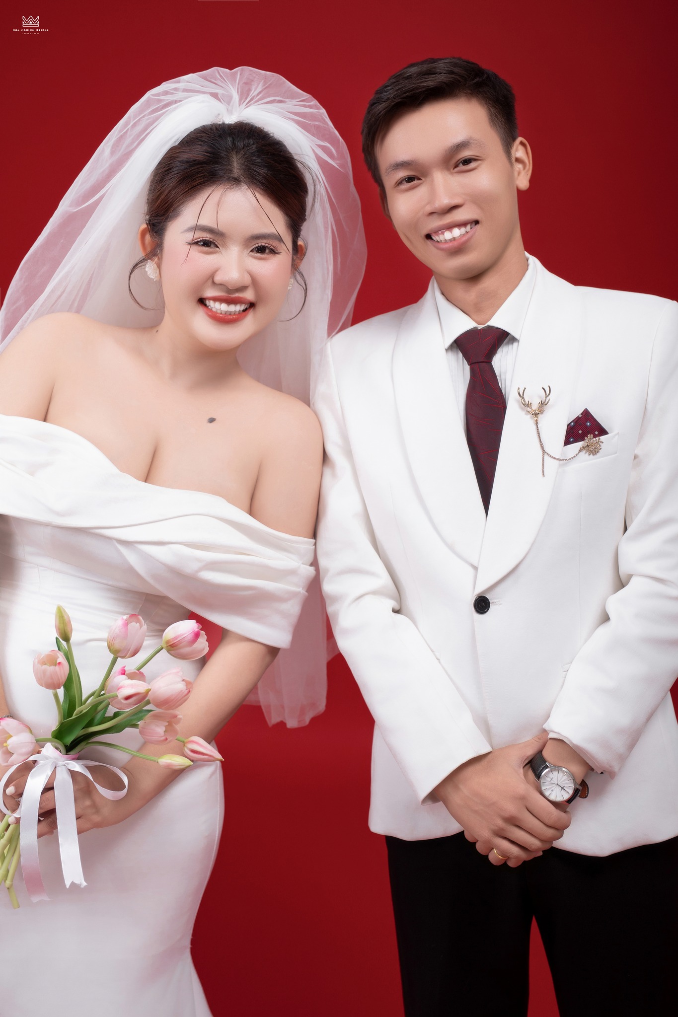 Cận cảnh cô dâu chú rể chụp ảnh cưới studio nền đỏ với nụ cười rạng rỡ