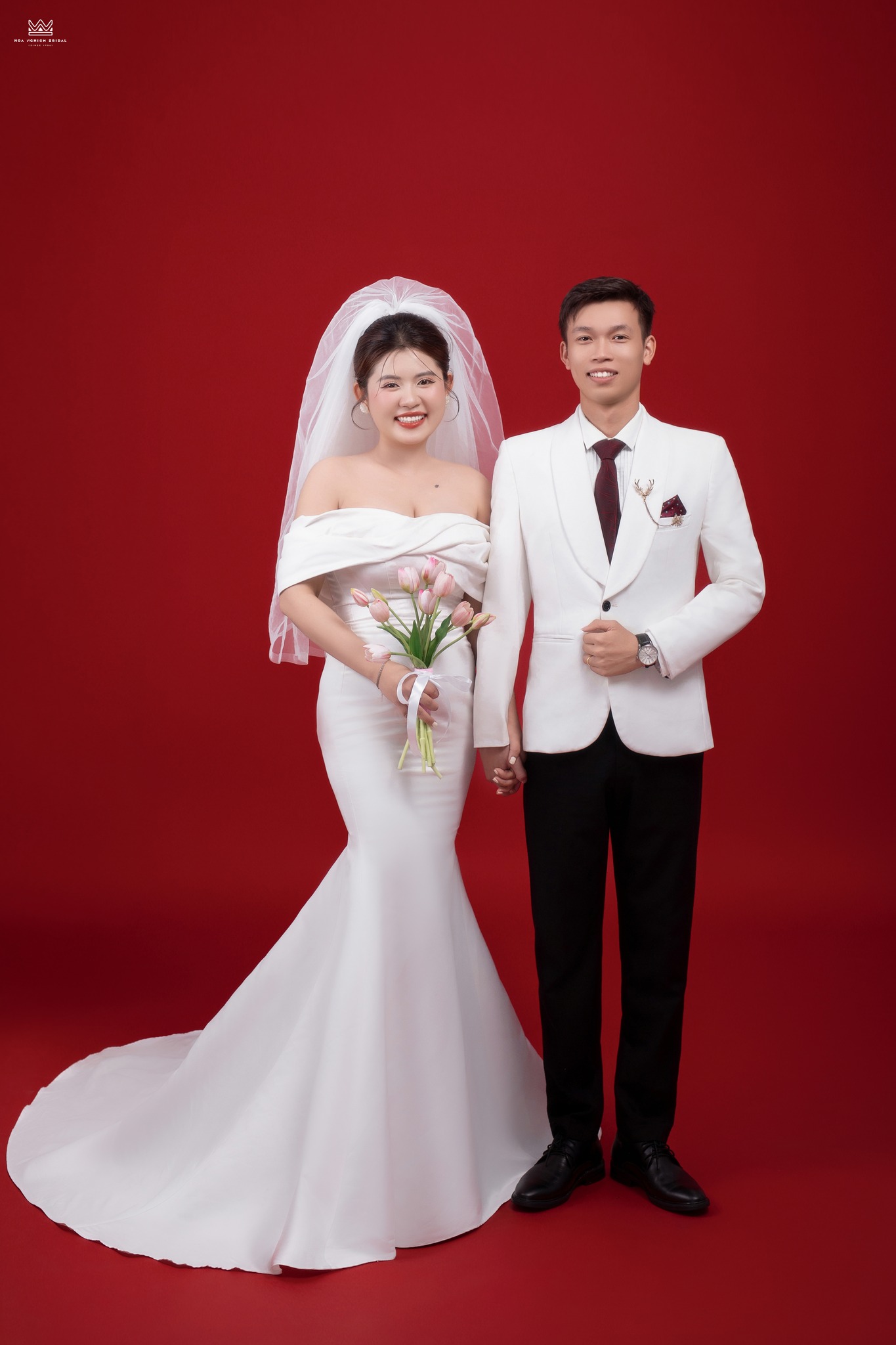 Cặp đôi chụp ảnh cưới studio đứng nghiêm chỉnh nắm tay nhau nền đỏ