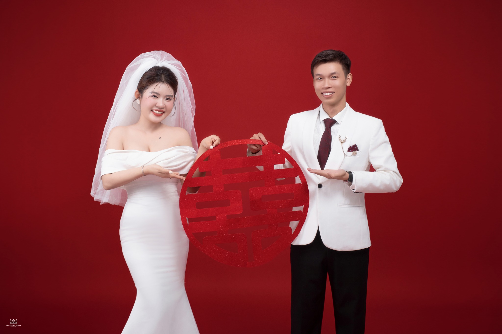 Ảnh cưới studio cô dâu chú rể cầm bảng song hỷ tròn nền đỏ