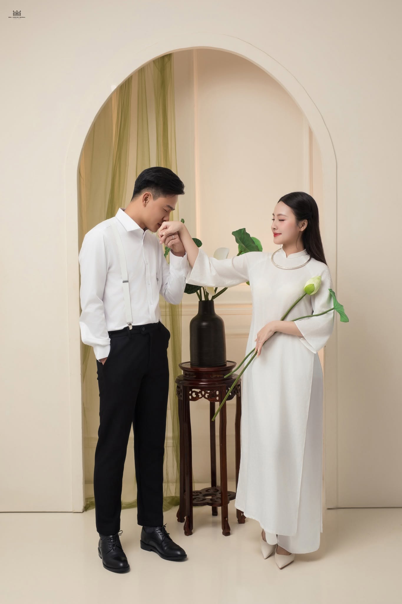 Khoảnh khắc chú rể hôn tay cô dâu trong concept áo dài trắng mang đến cảm xúc lãng mạn và tinh tế cho bộ ảnh cưới studio.