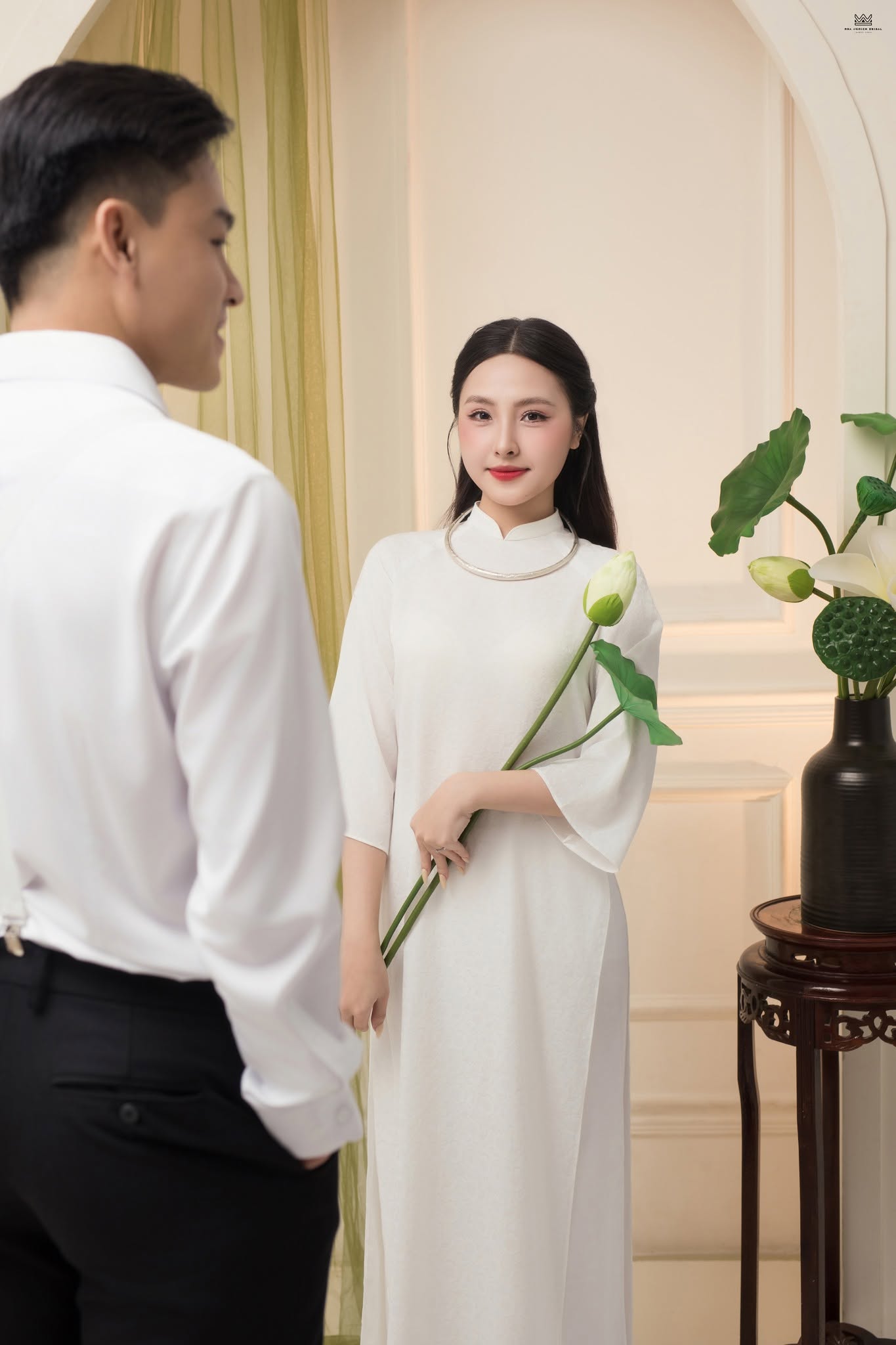 Hình ảnh cô dâu trong tà áo dài trắng cùng cành sen tạo nên vẻ đẹp dịu dàng, thanh lịch trong concept chụp ảnh cưới studio.